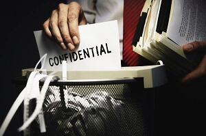 Image of man placing confidential document into paper shredder.