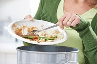 Image of woman scraping food waste off plate into trash.